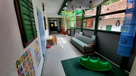 Ein Flur mit einer grünen Couch, einem Tisch und Stühlen. Der Raum hat grüne Fensterläden, einen Tisch und Stühle. Es gibt auch Dekorationen an der Wand.