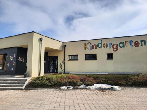 Die Vorderseite eines Kindergartengebäudes mit dem Wort Kindergarten darauf. Das Gebäude hat einen Ziegelboden und einige Pflanzen.