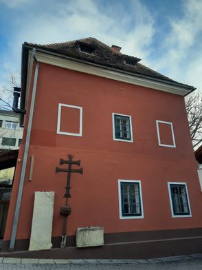 Ein rotes Gebäude mit weißen Fenstern und Rahmen, einem Kreuz an der Wand und einem Schornstein auf dem Dach.