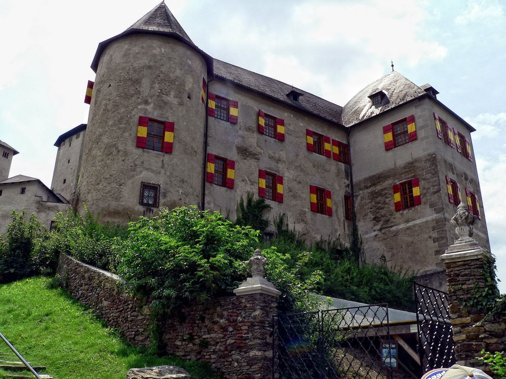  Abschnitt Bild: Eine große mittelalterliche Burg mit mehreren Fenstern, einige mit roten und gelben Fensterläden, auf einem Hügel mit einer grasigen Böschung.