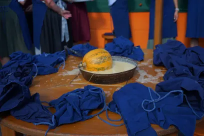 Ein Kürbis sitzt in einer Schüssel mit Teig auf einem Holztisch, umgeben von blauen Schürzen.
