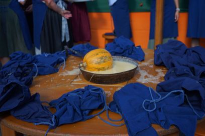 Ein Kürbis sitzt in einer Schüssel mit Teig auf einem Holztisch, umgeben von blauen Schürzen.