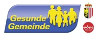 Blaues Banner mit gelben Silhouetten einer Familie, Text lautet 'Gesunde Gemeinden' mit einem Kronen- und Wappensymbol auf der rechten Seite.