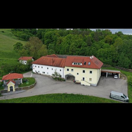 Eine Luftaufnahme eines großen Gebäudes mit rotem Dach und gelben Wänden, umgeben von einem grünen Rasen und Bäumen.