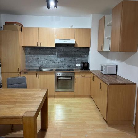 Eine moderne Küche mit Holzschränken, einem Herd, einer Mikrowelle und einem Esstisch. Es gibt eine Lampe an der Decke.