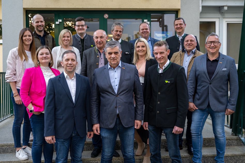 Eine Gruppe formell gekleideter Männer und Frauen steht auf den Stufen vor einem Gebäude. Sie lächeln für ein Foto.