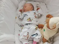 Ein Baby schläft in einem Kinderbett, trägt Winnie-the-Pooh-Pyjamas, mit einem rosa Socken und einem Kuscheltier in der Nähe.