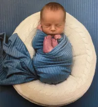 Ein Baby schläft friedlich in einer blauen Decke gewickelt auf einem gestrickten runden Kissen.