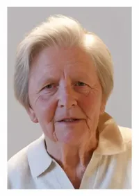 Eine ältere Frau mit kurzen weißen Haaren, einem ernsten Gesichtsausdruck und Falten um die Augen und den Mund. Sie trägt ein weißes Poloshirt.