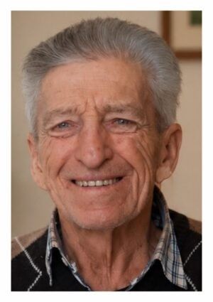 Ein älterer Mann mit grauem Haar und einem karierten Hemd lächelt. Er ist in einem Porträt mit weißem Hintergrund.