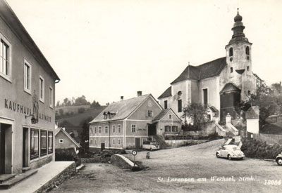 Schwarz-Weiß-Foto eines Dorfes mit einer Kirche und einem auf der Straße geparkten Auto. Die Kirche hat einen hohen Turm und ein Schild, das St. Lorenzen am Wechsel liest.